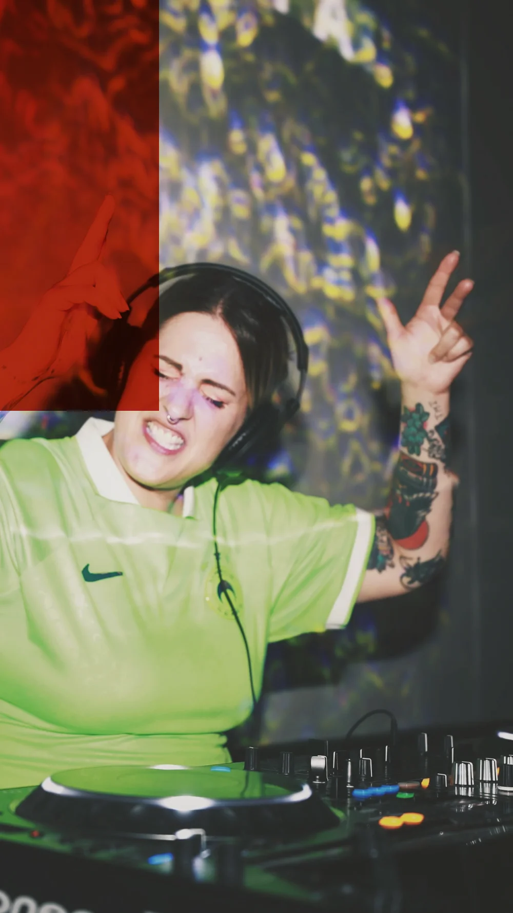 A DJ in a green shirt with her arms up, projections behind her