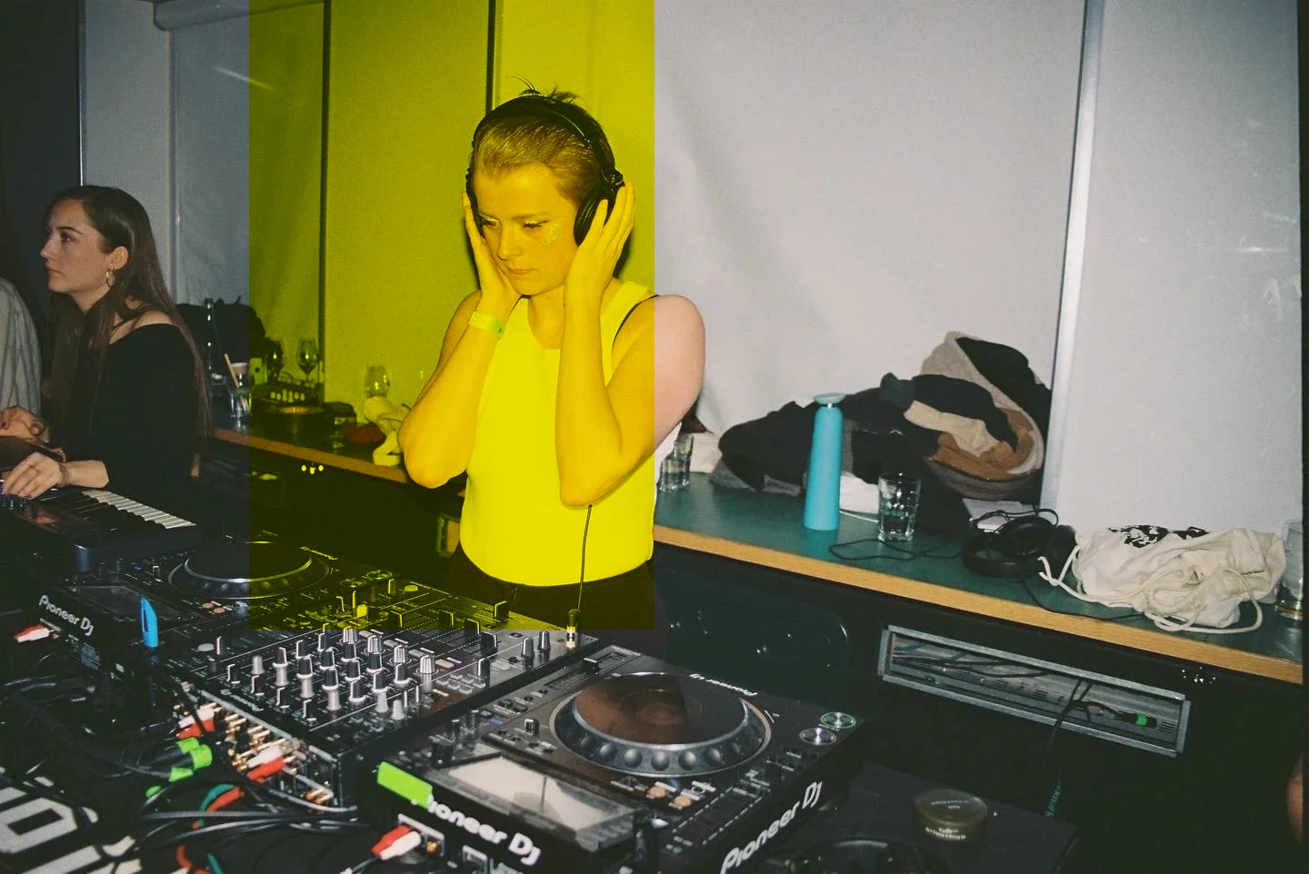A DJ in headphones at the decks, with a white wall behind