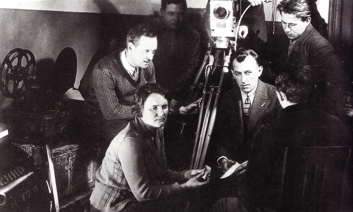 Black and white photograph of Yelizaveta Svilova holding a strip of film, with a film crew and a camera behind her
