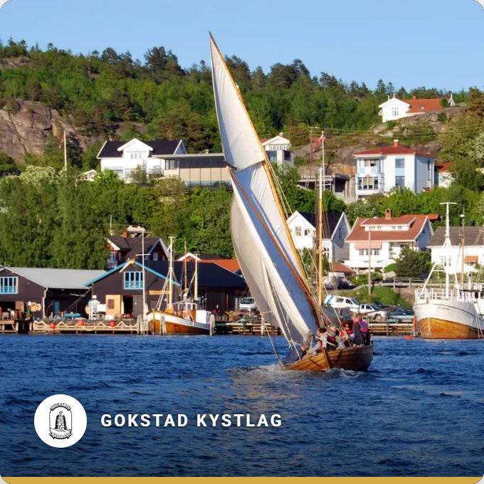 Gokstad Kystlag: a wooden sailing boat with a white sail in front of the harbour in Sandefjord