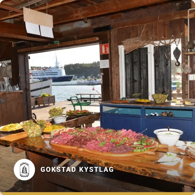 Gokstad Kystlag: a long table with food in a wooden hall with a view of the harbour