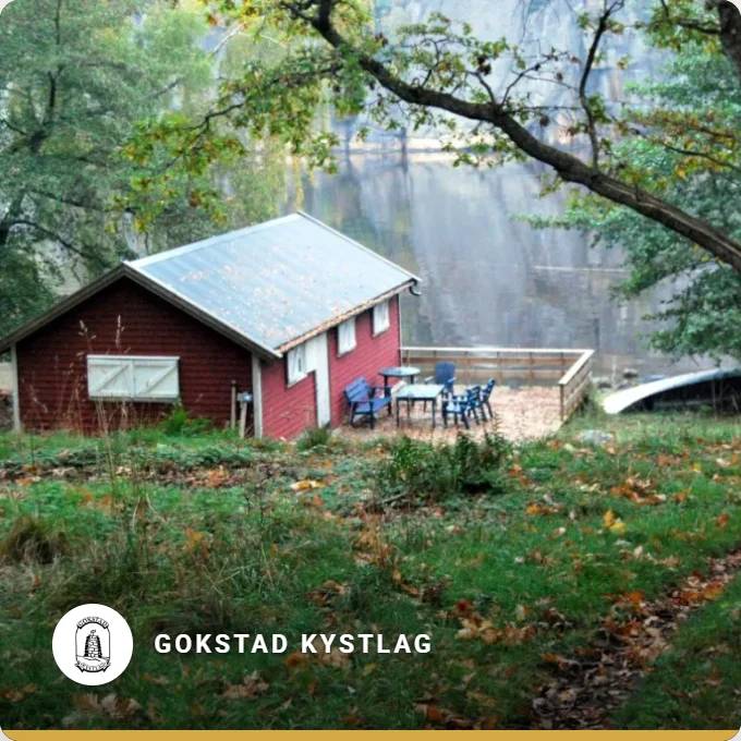 Gokstad Kystlag: a red boathouse among green trees by the water